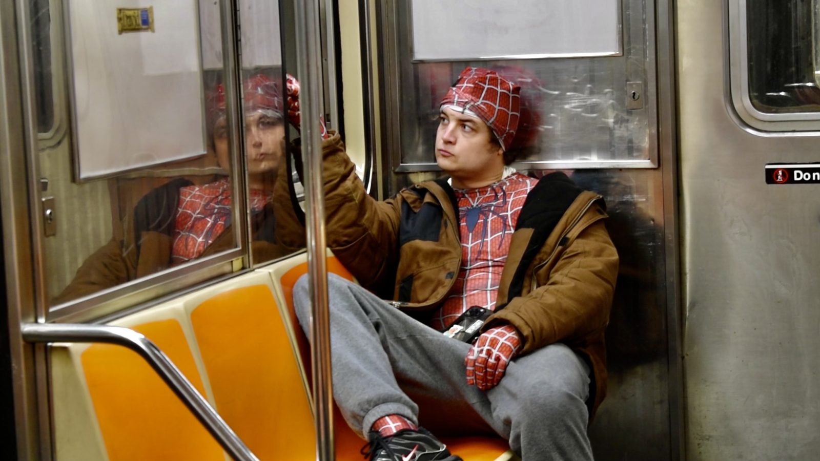 Still from Being a Hero: Kemp on the subway in a costume and brown jacket